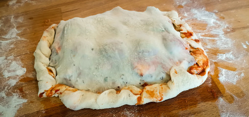 Calzone roh auf Holzbrett mit Mehl