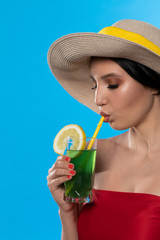 A young woman drinks a drink on a hot summer day and has a hat on her head.