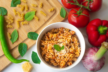 Italian pasta fusilli with fresh and spicy tomato sauce, Parmesan cheese and basil with ingredients in the background - tomatoes, garlic, paprika, dry pasta, Parmesan cheese and basil leaves