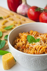 Italian pasta fusilli with fresh and spicy tomato sauce, Parmesan cheese and basil with ingredients in the background - tomatoes, garlic, paprika, dry pasta, Parmesan cheese and basil leaves