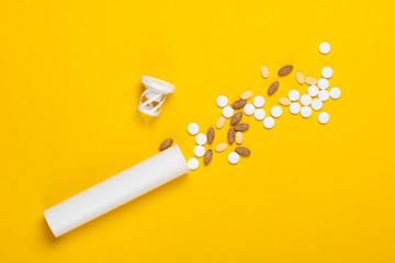 Bottle with different pills on yellow background.