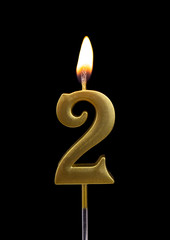 Burning birthday golden candle isolated on black background, number 2