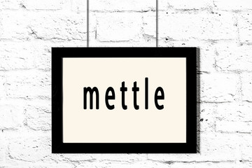 Black frame hanging on white brick wall with inscription mettle