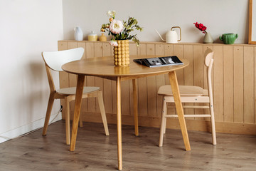 Wooden dining table in a bright home interior. On the table are peonies in a designer yellow vase .