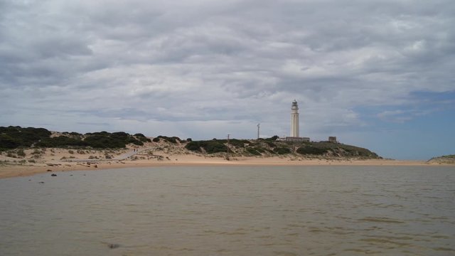 faro en la playa con agua por delante un dia soleado con nubes