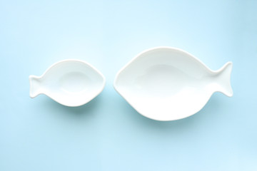 White ceramic empty plates in the shape of fish large and small on a blue background. Selective focus. Table setting.