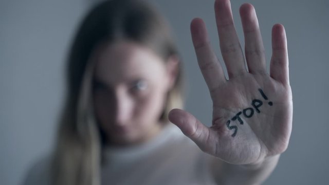 Woman with bruises on her face showing stop sign, palm in focus
