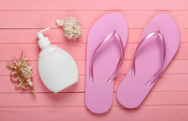 Beach vacation concept, summer background. Flip flops with bottle of sunblock, seashell on pink...