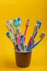 Lot of old used toothbrushes in cup on yellow background