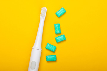 Electric Toothbrush with chewing gum on a yellow background. Caring for dental health, fresh breath