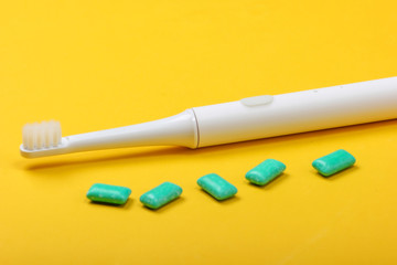 Electric Toothbrush with chewing gum on a yellow background. Caring for dental health, fresh breath