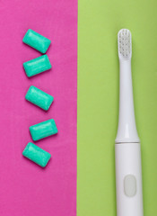 Electric Toothbrush with chewing gum on pink green background. Caring for dental health, fresh breath. Top view