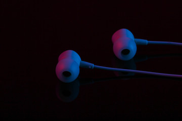 Blue vacuum earphones in red neon light on black background close-up