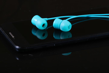 Blue vacuum earphones with smartphone on a black background close-up