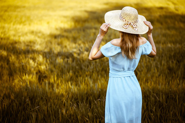 Young woman in hat standing on the wheat field with sunset on the background