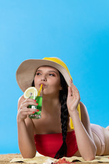 A young teenager is lying on the beach with an alcoholic drink and sunbathing in the summer sun.