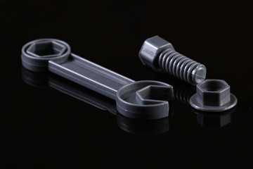 Gray plastic wrench with nut and bolt on a black background