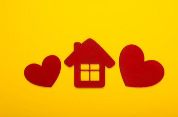 Red wooden hearts with a house figurine on a yellow background