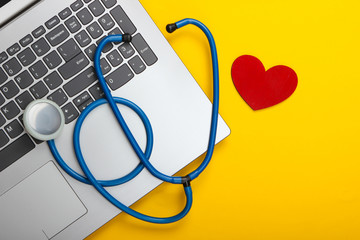 Laptop and stethoscope with heart on yellow background. Top view