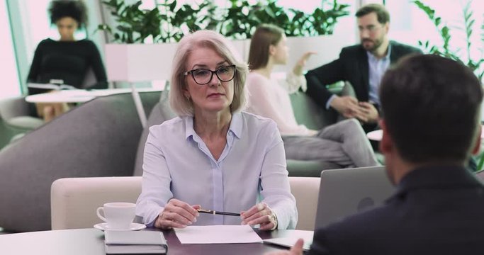 Confident middle aged female recruiter sitting in front of job applicant, listening to self presentation in modern working space. Skilled mature company leader executive talking to motivated employee.