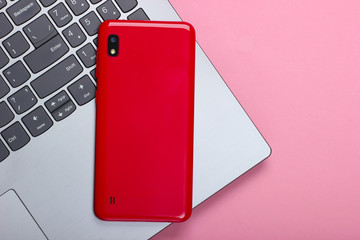 Laptop with smartphone on a pink pastel background. Top view