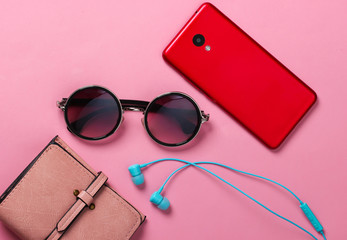 Women's accessories and gadgets on a yellow background. Earphones, stylish round sunglasses, smartphone, wallet on pink background