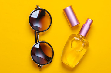 Fashionable round sunglasses and perfume bottle on yellow background. Top view