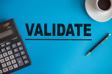 The word VALIDATE is written on a blue background next to a calculator, pen, and coffee Cup