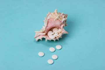 Mineral tablets (calcium) with seashells on a blue background