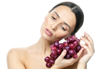 close-up portrait of a girl with clear skin and big brown eyes with soft makeup, with red grapes on a white background