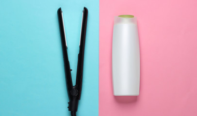 Set of products and devices for hair care. Hair straightener with a bottle of shampoo on a blue-pink pastel background. Top view