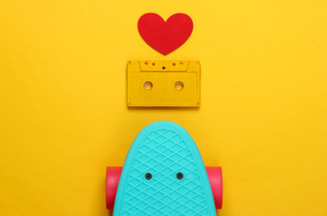 Cruiser board and retro audio cassette, heart on yellow background. 80s. Top view. Minimalism.