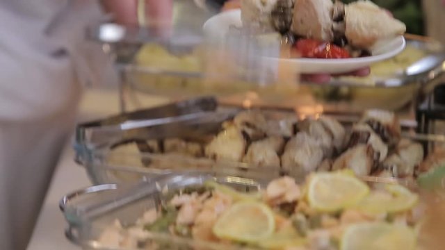 Close up view human hands putting on plate snacks at stand up wedding buffet.  Catering in the proccess.