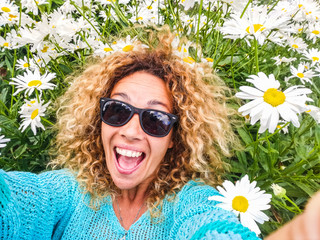 Happy cheerful and beautiful adult caucasian woman enjoy the nature lay down in a daisy flowers meadow for spring and joyful people concept - pretty lady in selfie picture view