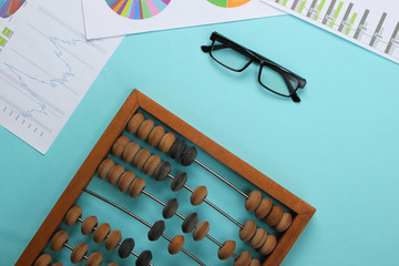 Abacus with graphs and charts, glasses on blue pastel background. Top view.