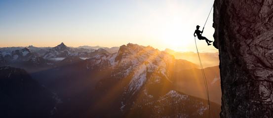 Silhouette Rappelling from Cliff. Beautiful aerial view of the mountains during a colorful and...