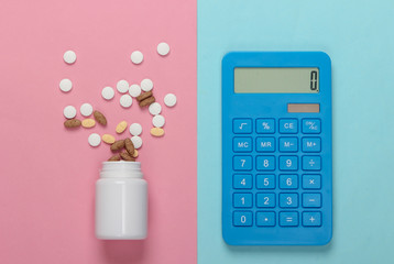 Bottle with different pills and calculator on a blue pink background. Top view