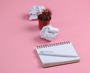Crumpled paper balls, cactus pot and notepad on pink pastel background. Working space