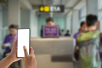 Woman passenger hand holding empty screen of smart phone and check-in counter airport terminal background.