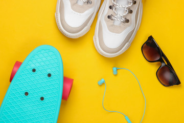 Fashionable sneakers with cruiser board, sunglasses, earphones on yellow background. Youth fun. Top...