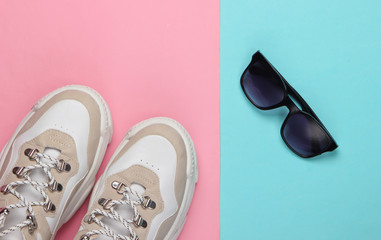 Fashionable sneakers with sunglasses on pink blue pastel background. Top view. Minimalism