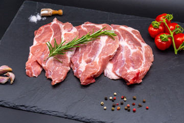 pork raw steak and ingredients on black slate