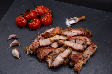 pork steak on black slate and grilled tomatoes and salt