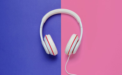 Classic white headphones on blue pink paper background. Retro style. 80s. Pop culture. Top view. Minimal Music Concept