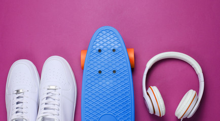 Hipster outfit. Skateboard with headphones and sneakers on purple background. Creative fashion minimalism. Trendy old fashionable style. Minimal summer fun. Music concept
