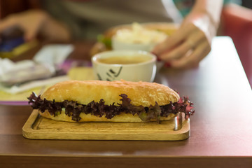 Ciabatta sandwich with ham, cheese, cucumber and lettuce, cup of coffee and for breakfast. Selective focus