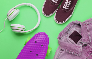 Hipster fashion look. Denim jacket, skate, sneakers, headphones on green background. Top view. Flat lay