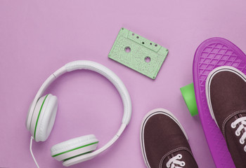 Hipster outfit. Skateboard with headphones, audio cassette and sneakers on pink background. Creative fashion minimalism. Minimal summer fun. Pop art. 80s. Top view