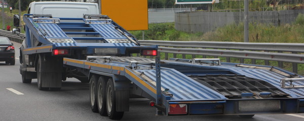 Naklejka premium Empty car carrier truck with three-axle car transporter trailer drive on industrial area road, rear side wide view close up, delivery autos logistics, automobile transportation