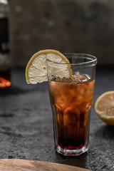 A glass of rum with cola full of ice with a slice of lemon on a dark background and copyspace. Alcoholic cocktail